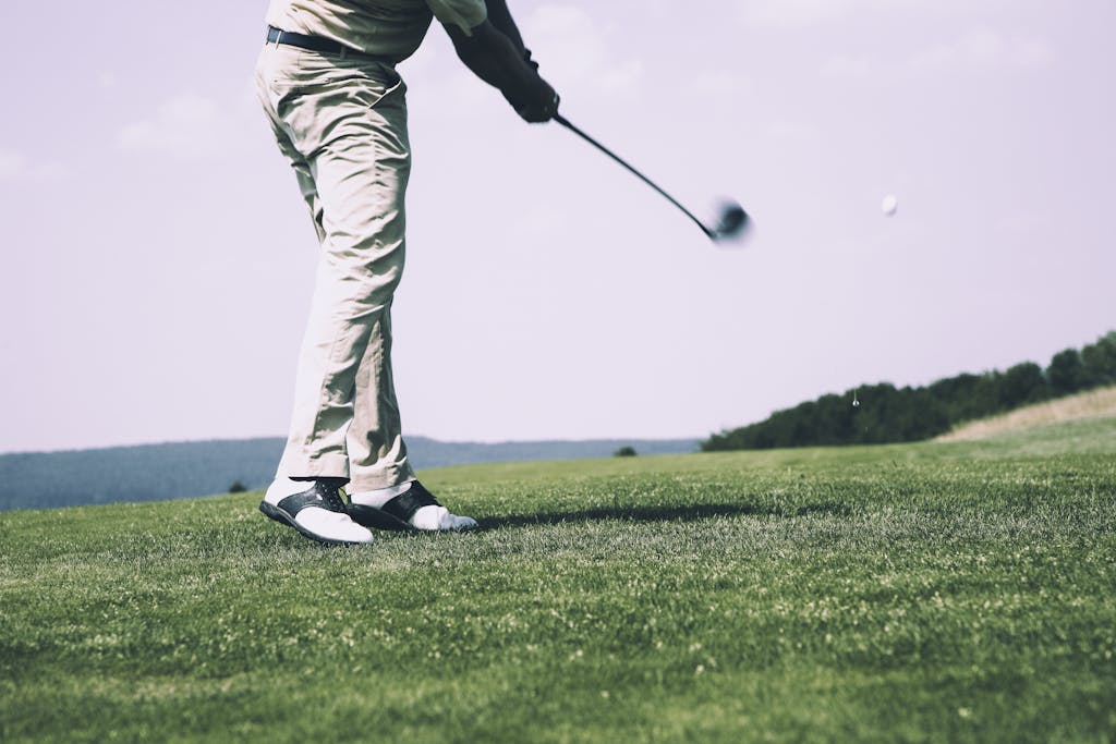 A golfer in mid-swing on a sunny day at the golf course, showing motion and focus.