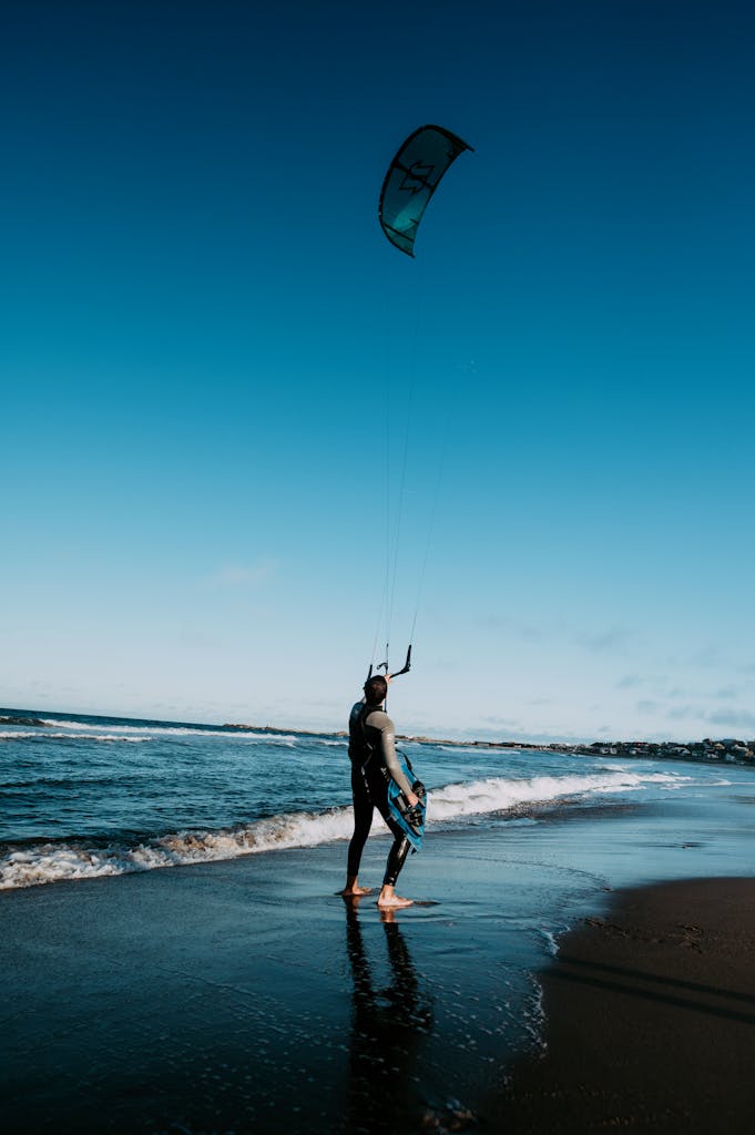 Kitesurfer getting ready on a sandy beach with clear blue skies.
