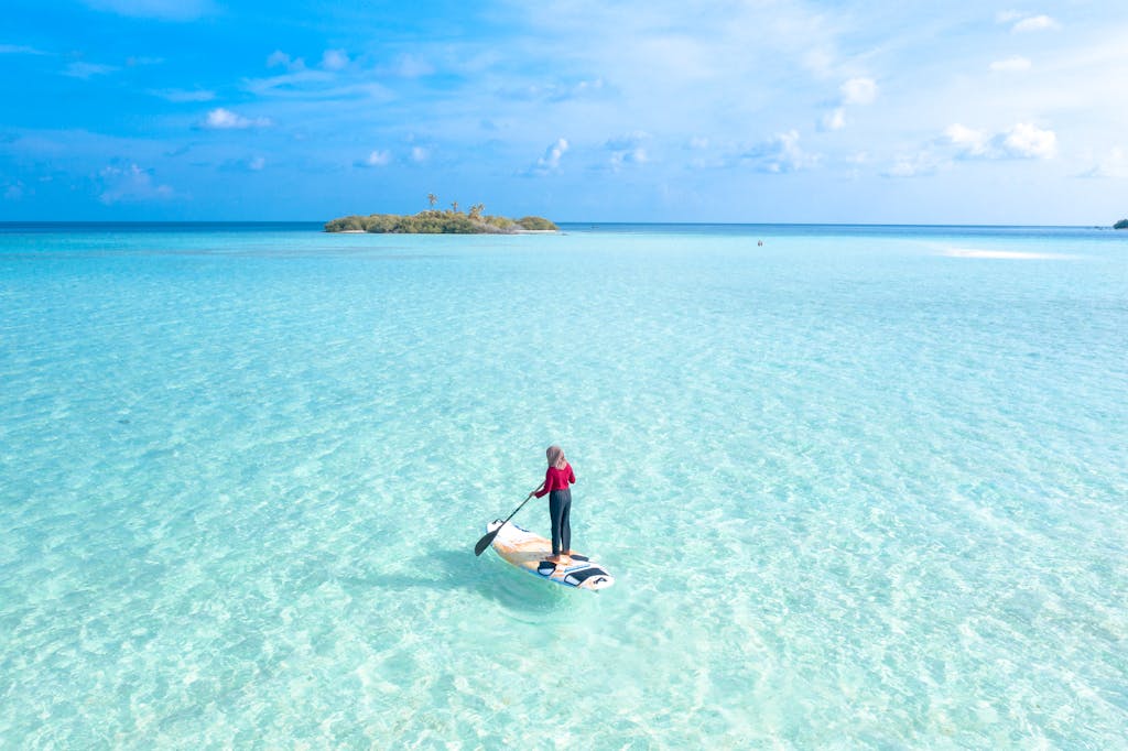 Aerial shot of a person paddleboarding in clear turquoise water near a small tropical island.