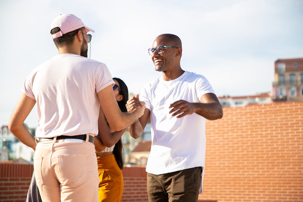 Happy smiling multiethnic male friends greeting each other and shaking hands while gathering on rooftop in urban city