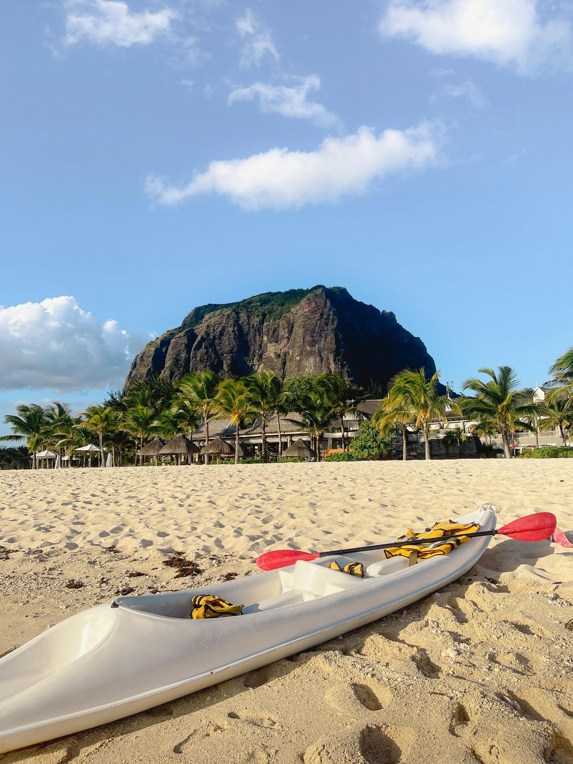 Serene beach with a canoe, palm trees, and the iconic Le Morne Brabant mountain in Mauritius.